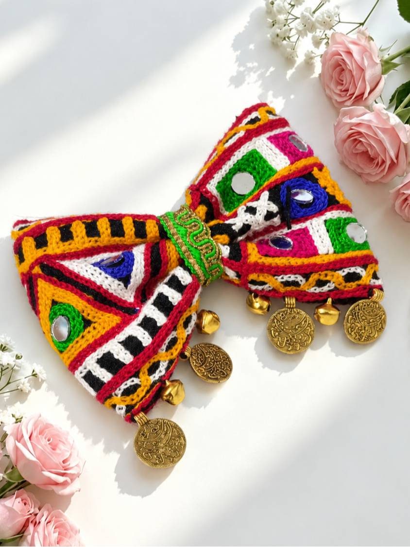 Colourful Kutchi embroidered bow hair clip with mirror work, ghungroo bells and gold-toned coin charms on white background with pink roses