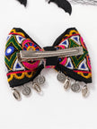 Back view of embroidered bow hair clip showing silver alligator clip base and dangling coin and cowrie charms