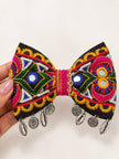 Hand holding embroidered mirror work bow hair clip showing full front detail with multicolour threadwork and danglers