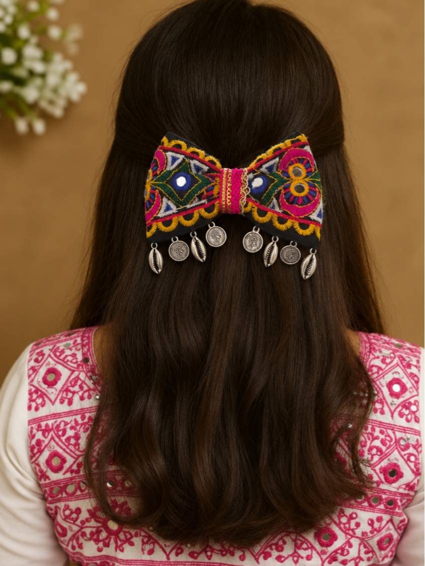 Embroidered bow hair clip worn in a half-up hairstyle on a woman in a pink mirror work top, showing scale and styling