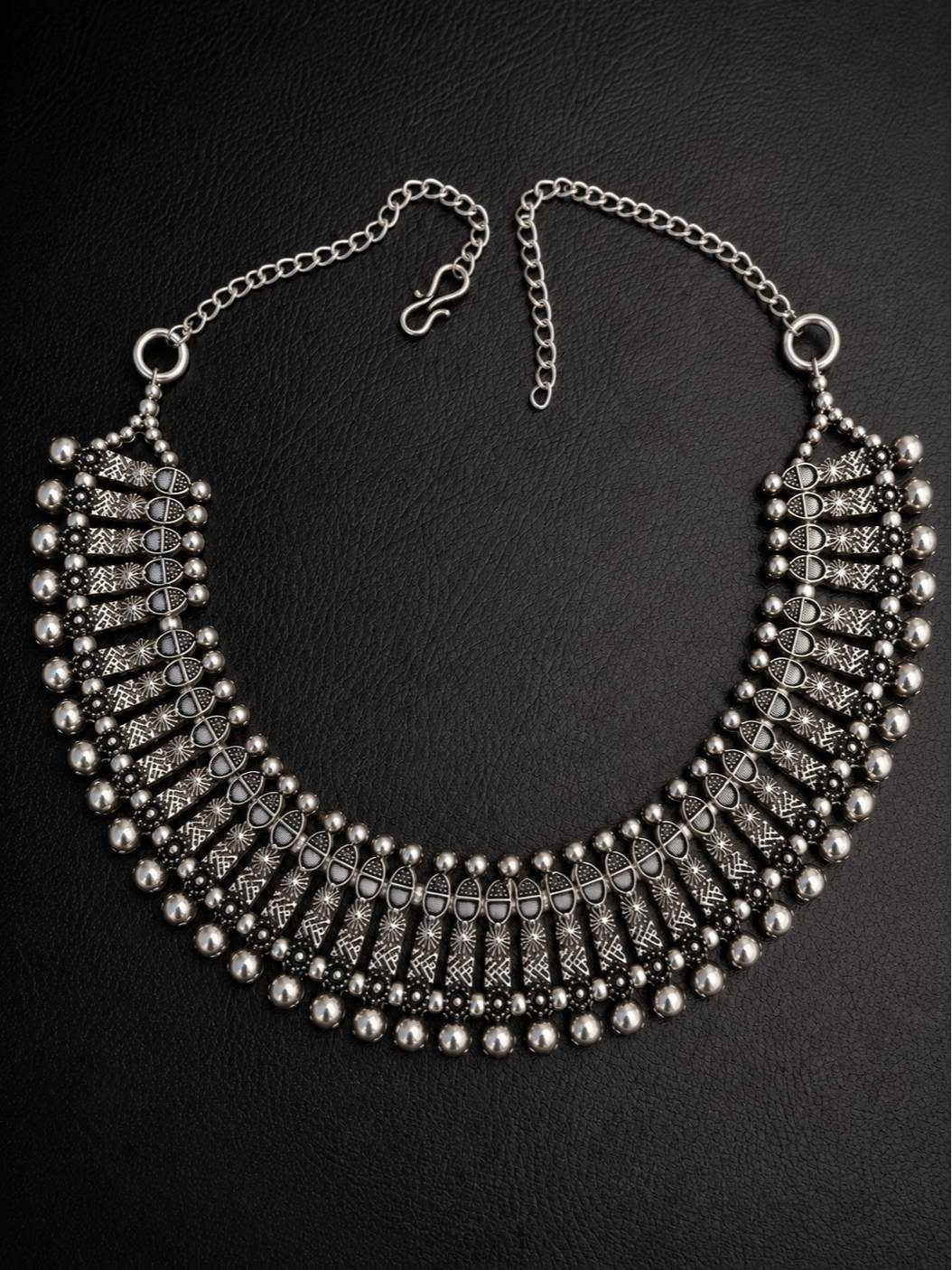 Flat lay of oxidised silver tribal choker necklace on dark background with S-hook extender chain visible