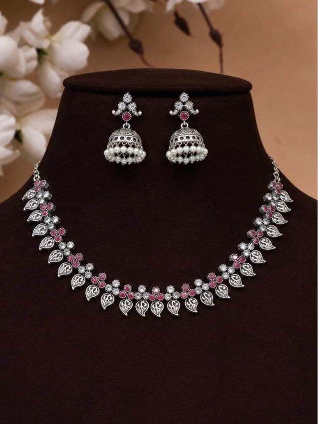 Oxidised silver leaf necklace set with ruby stone flowers and jhumka earrings displayed on dark jewellery bust
