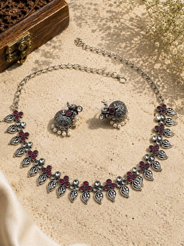 Flat lay of oxidised silver leaf necklace and jhumka earrings on sandy surface beside wooden jewellery box