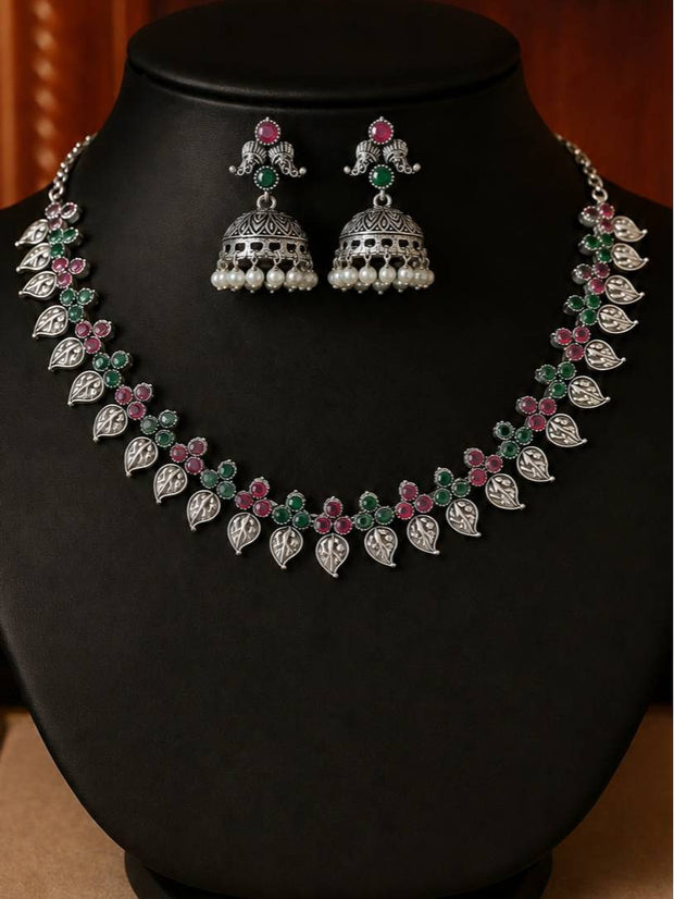 Oxidised silver leaf necklace and jhumka set displayed on a black jewellery bust with ruby and emerald stones