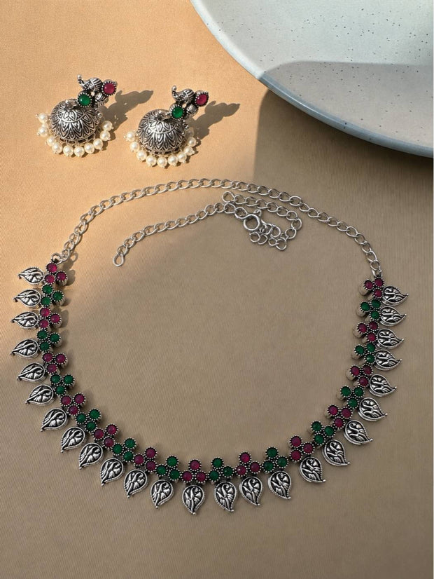 Flat lay of oxidised silver leaf necklace with adjustable chain and matching jhumka earrings on a beige surface