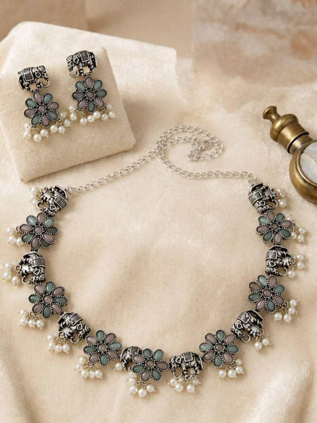 Oxidised silver floral necklace and jhumka earrings flatlay on cream fabric with vintage brass prop