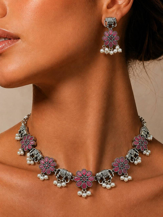 Woman wearing oxidised silver elephant flower necklace and matching pink stone earrings against a warm beige background