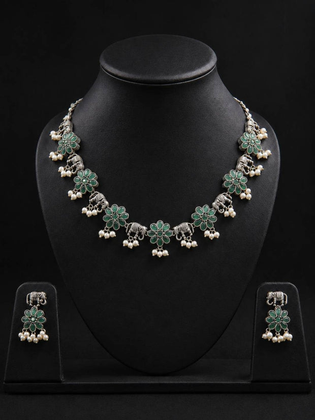 Oxidised silver elephant flower necklace set with green stones and pearl drops displayed on a black jewellery bust with matching earrings