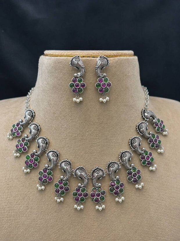 Oxidised silver elephant choker necklace set with ruby and green stone floral pendants displayed on a jewellery bust