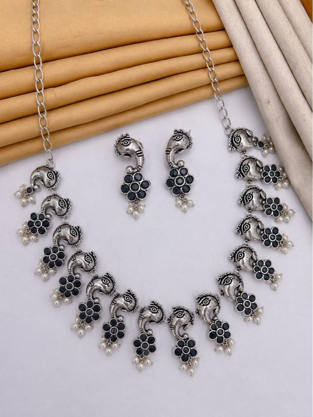 Oxidised silver elephant necklace set with dark blue stone floral pendants and pearl drops laid flat on white surface