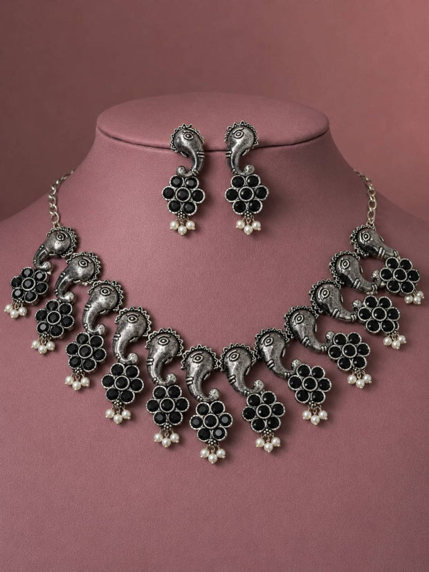 Oxidised silver peacock choker necklace and earring set displayed on a jewellery bust against a dusty rose background