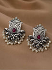 Pair of oxidised silver lotus stud earrings with ruby-red teardrop stone and white pearl drops, laid flat on beige fabric