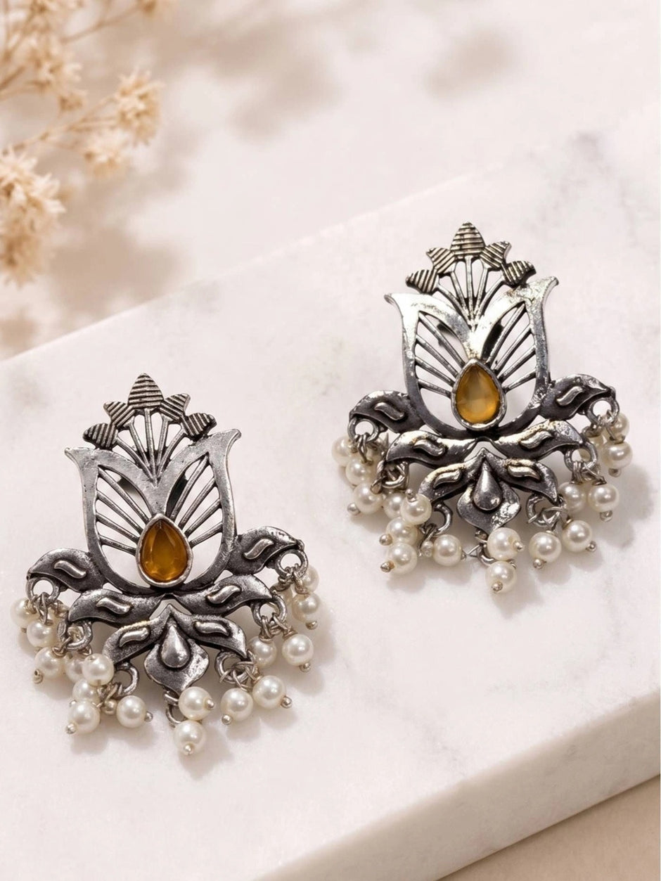 Pair of oxidised silver lotus stud earrings with amber stone and white pearl drops on marble surface