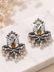 Pair of oxidised silver lotus stud earrings with amber stone and white pearl drops on marble surface