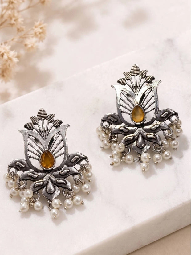 Pair of oxidised silver lotus stud earrings with amber stone and white pearl drops on marble surface