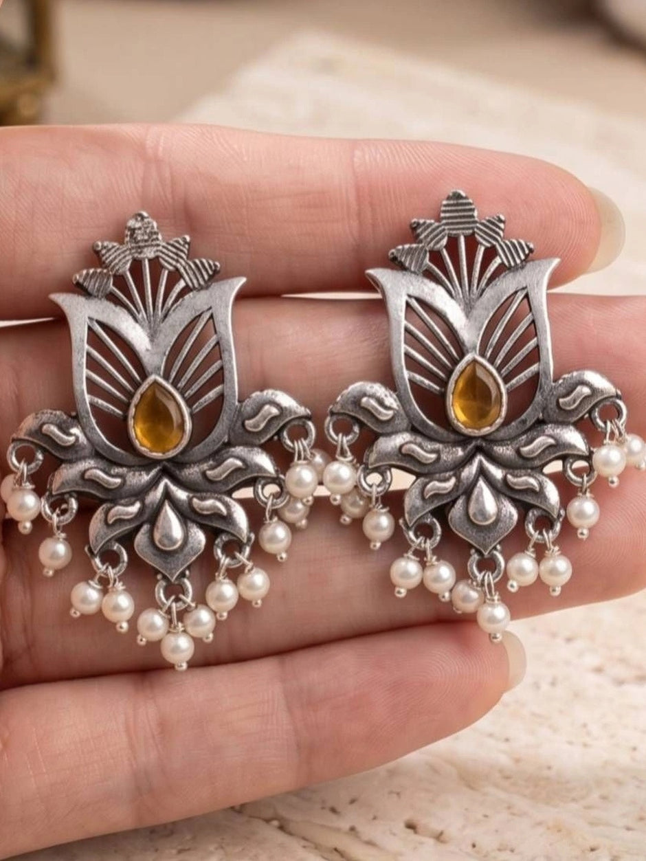 Close-up of two oxidised silver lotus earrings with amber stone centres and pearl drops held in palm