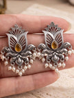 Close-up of two oxidised silver lotus earrings with amber stone centres and pearl drops held in palm