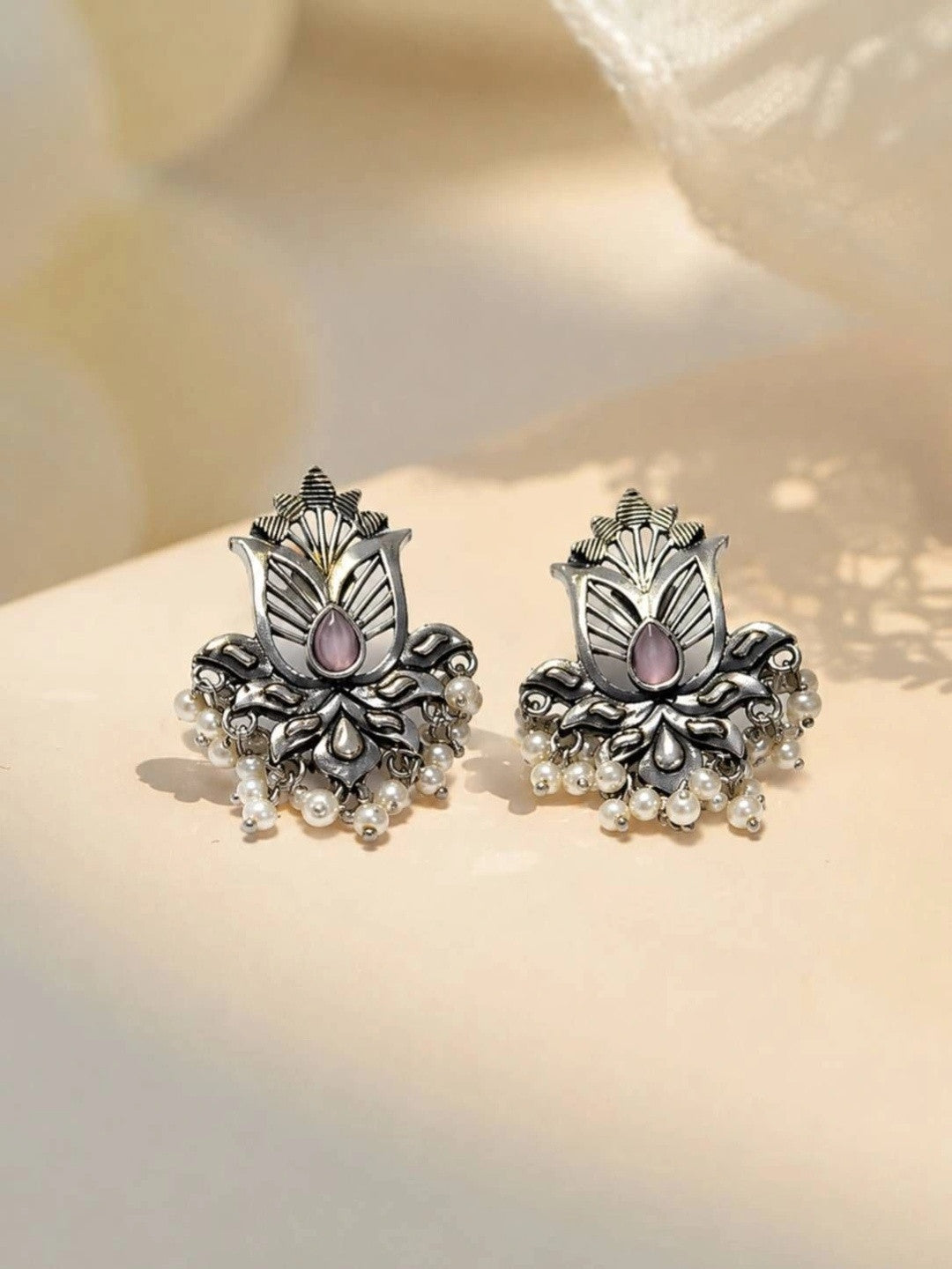 Pair of oxidised silver lotus stud earrings with pink teardrop stone and white pearl drops on cream surface