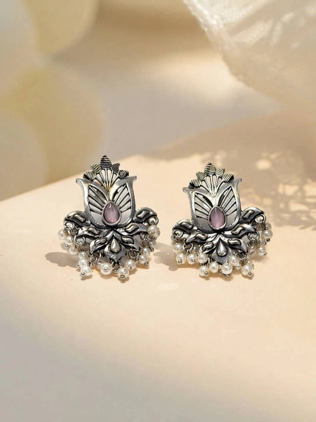 Pair of oxidised silver lotus stud earrings with pink teardrop stone and white pearl drops on cream surface
