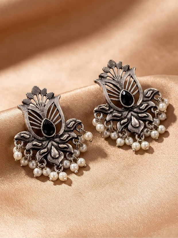 Pair of oxidised silver lotus stud earrings with black teardrop stone and white pearl drop fringe on peach fabric
