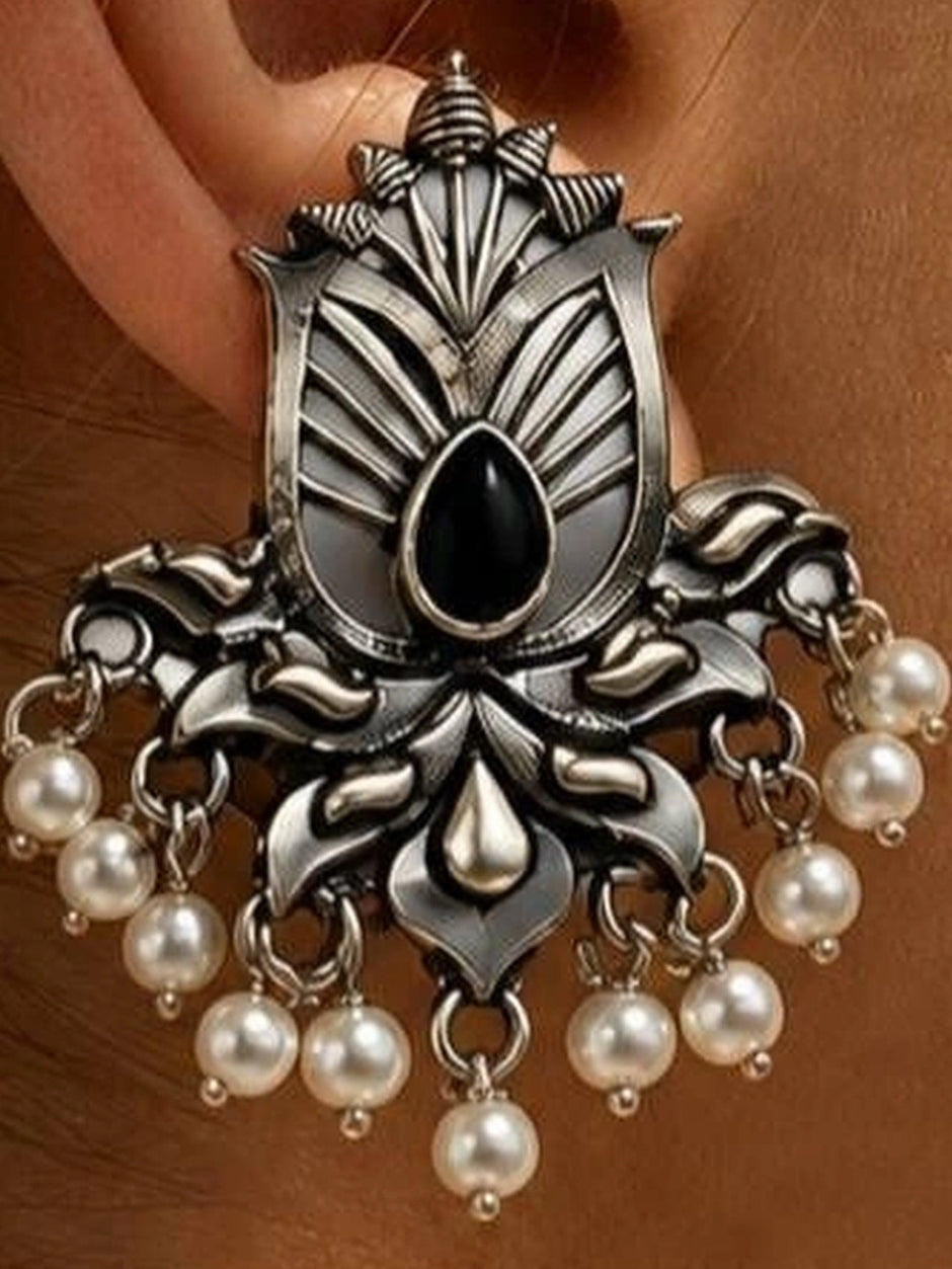 Close-up of oxidised silver lotus earring worn on ear showing engraved floral detail, black stone and pearl drops