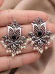 Two oxidised silver lotus stud earrings held in a palm showing open-cut design, black centre stone and pearl fringe