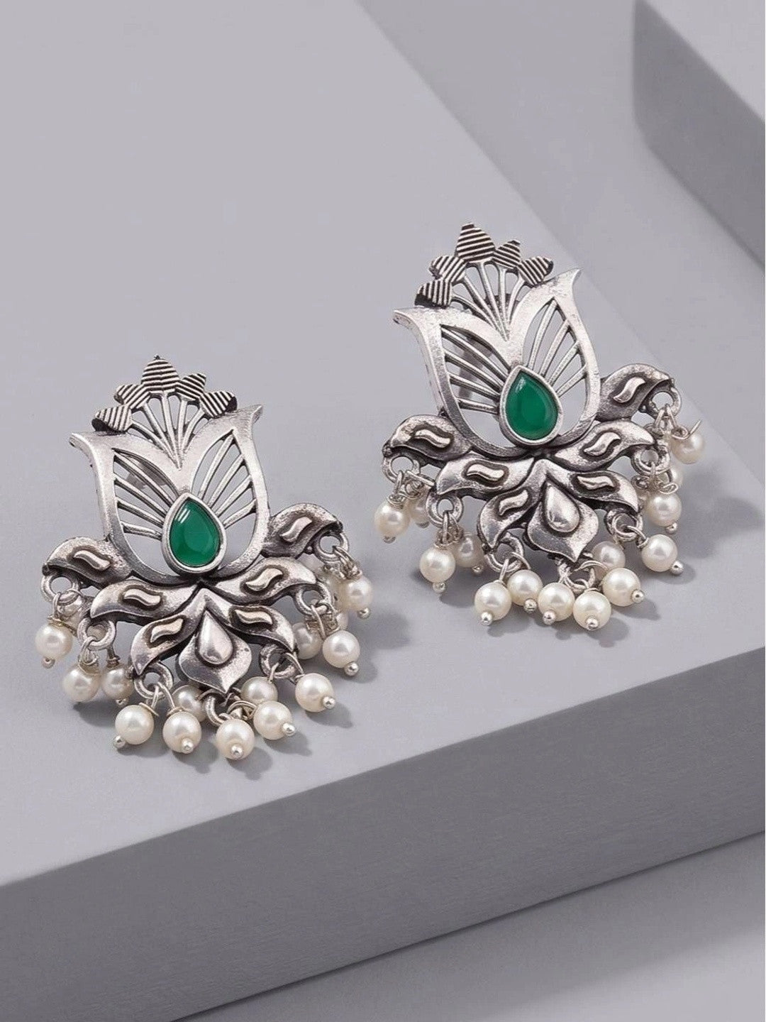 Pair of oxidised silver lotus stud earrings with green teardrop stone and ivory pearl drops, front view on grey surface