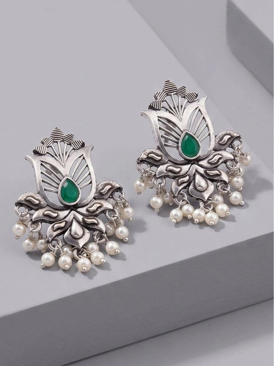 Pair of oxidised silver lotus stud earrings with green teardrop stone and ivory pearl drops, front view on grey surface