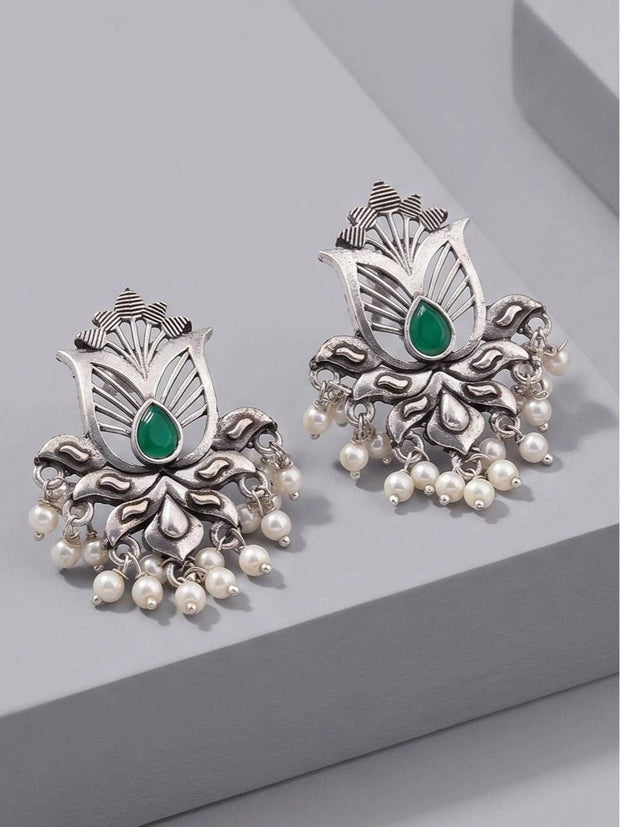 Pair of oxidised silver lotus stud earrings with green teardrop stone and ivory pearl drops, front view on grey surface