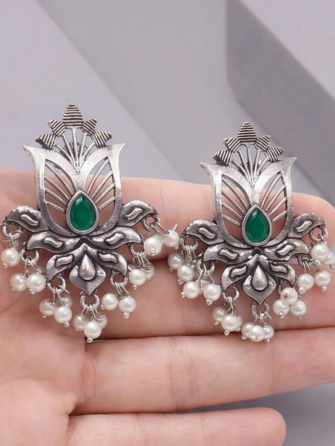 Both oxidised silver lotus earrings resting on an open palm, showing full design with green stone and pearl fringe