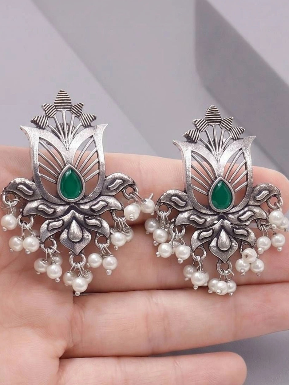 Both oxidised silver lotus earrings resting on an open palm, showing full design with green stone and pearl fringe