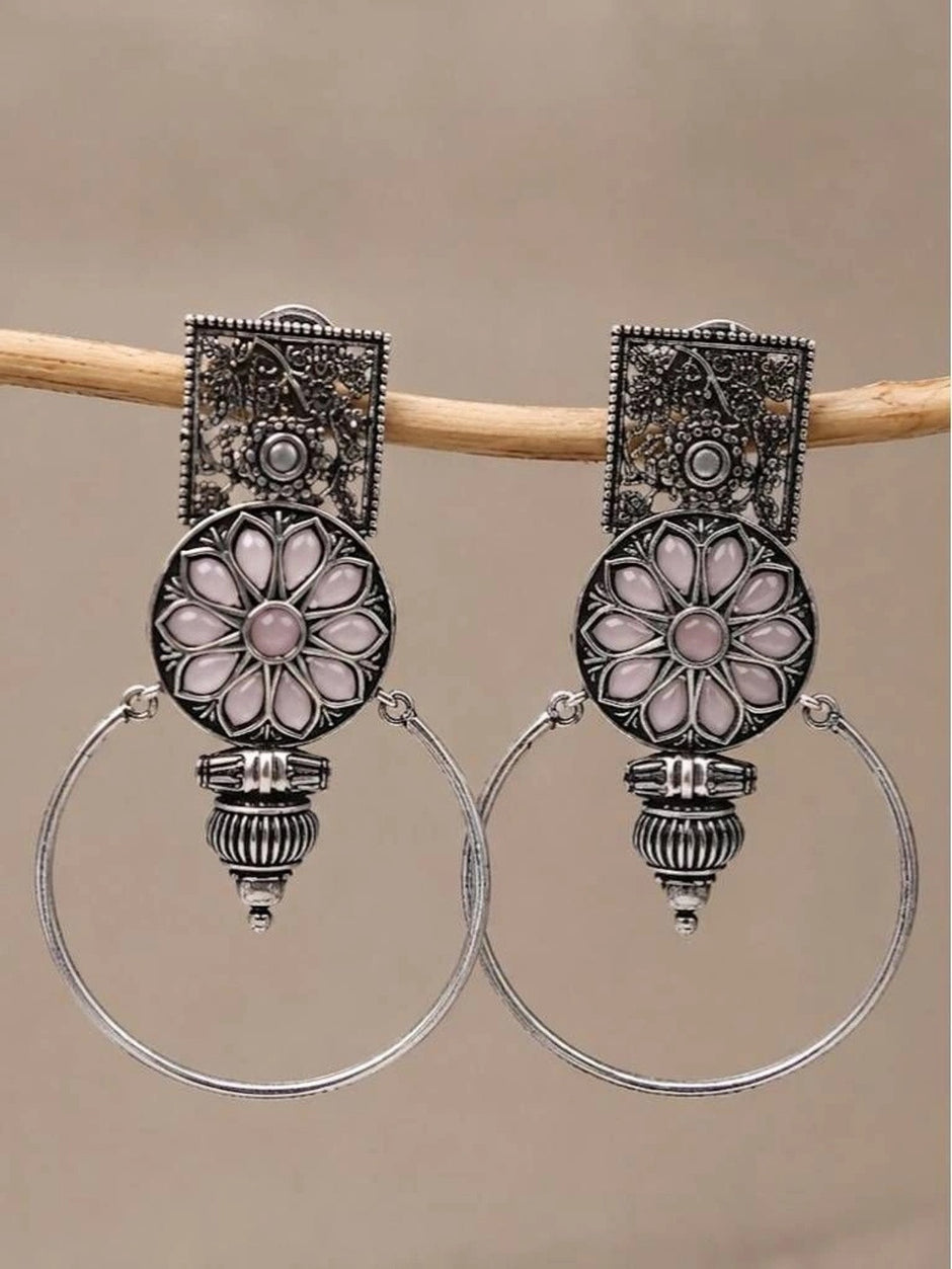 Pair of oxidised silver floral hoop earrings with pink resin stones hanging on a wooden rod