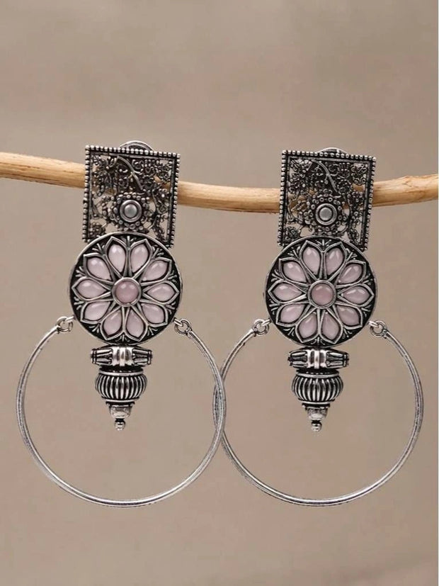 Pair of oxidised silver floral hoop earrings with pink resin stones hanging on a wooden rod