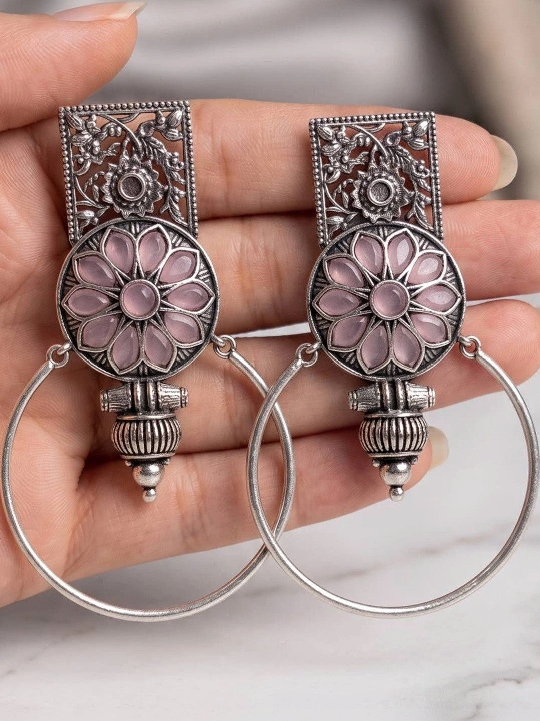 Close-up of both oxidised silver floral hoop earrings resting on an open palm showing pink stone detail