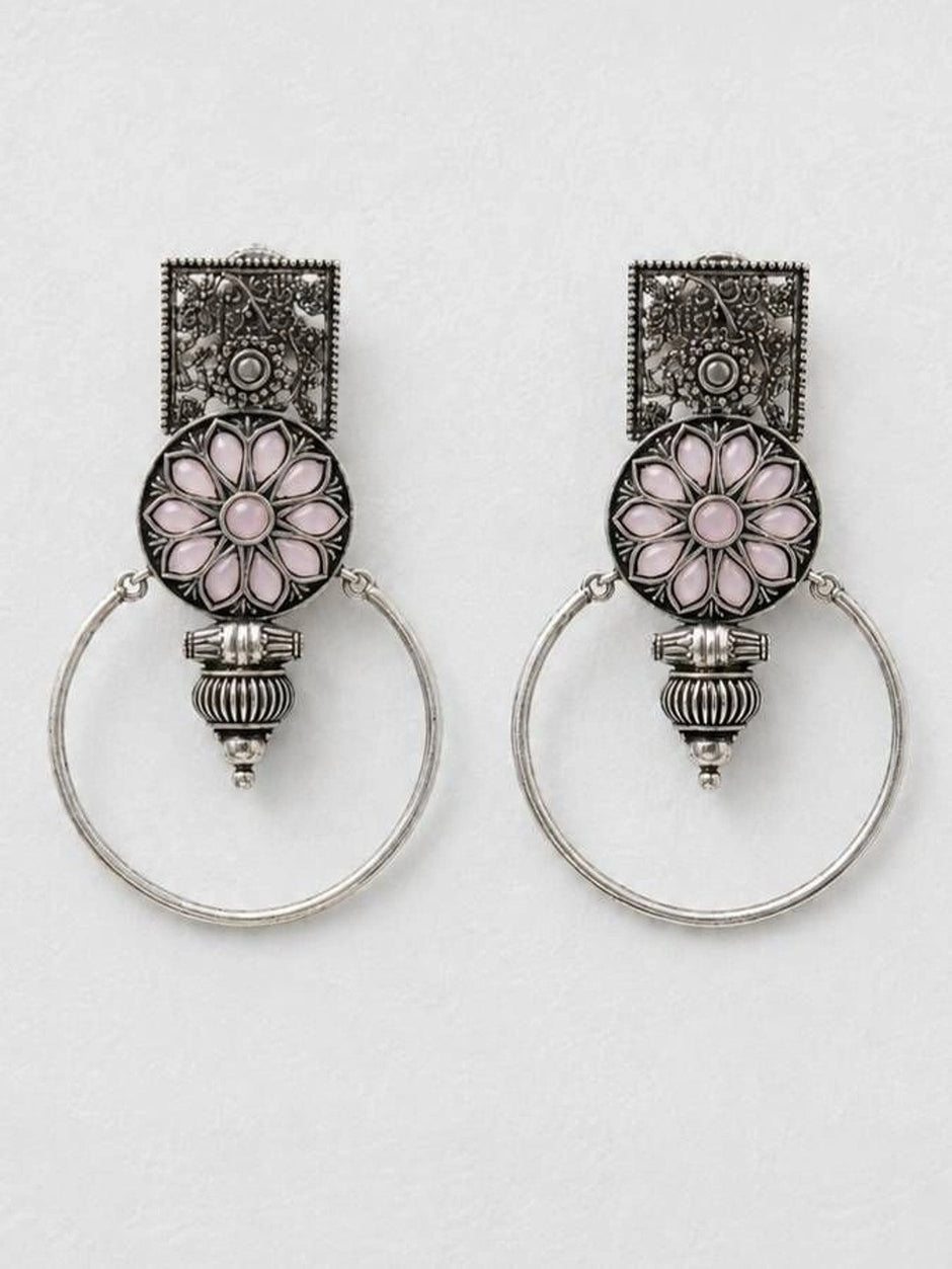 Pair of oxidised silver floral hoop earrings laid flat on a white marble surface