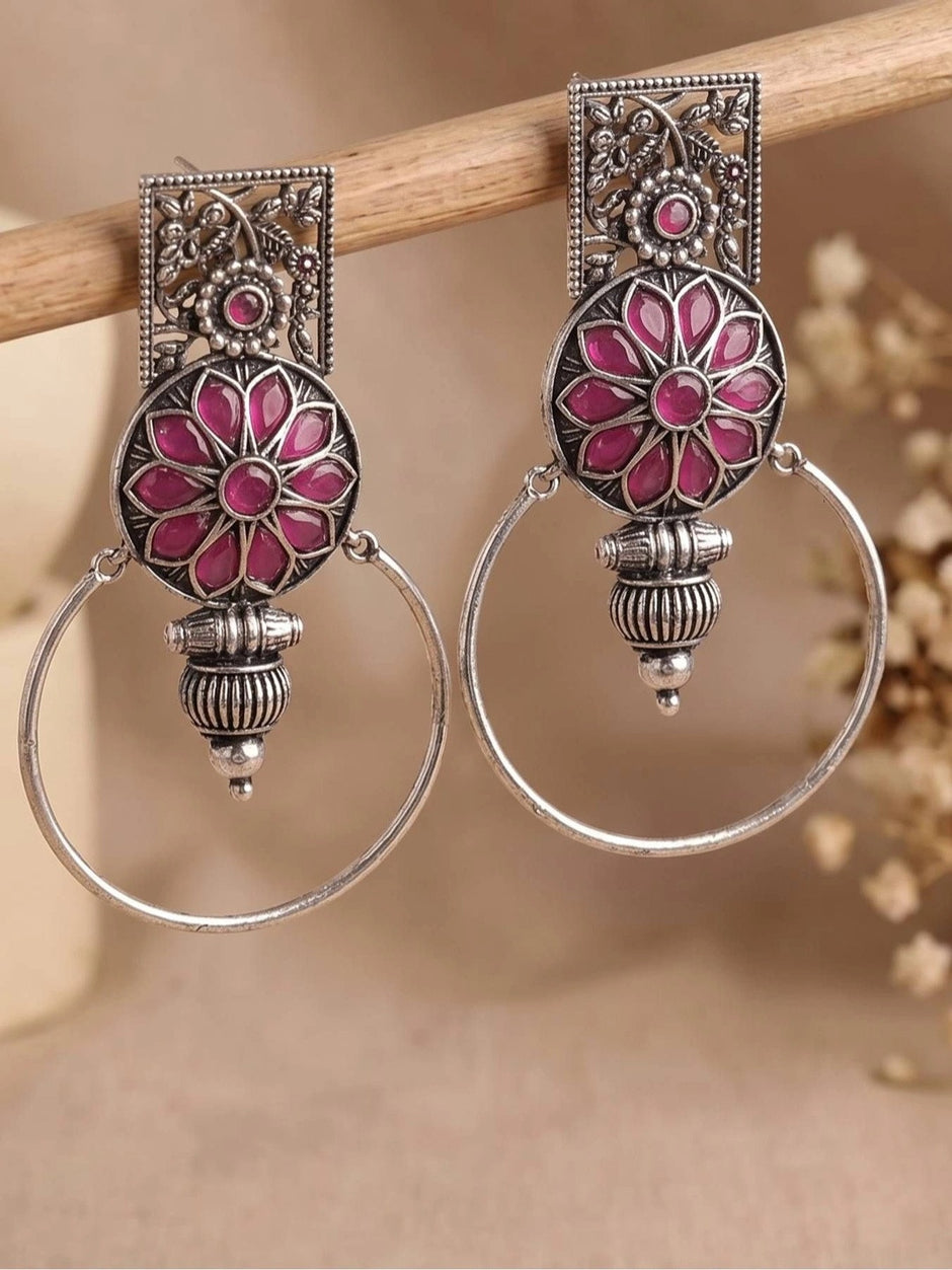 Pair of oxidised silver hoop earrings with magenta floral medallion hanging on a wooden rod