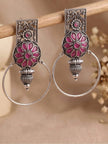 Pair of oxidised silver hoop earrings with magenta floral medallion hanging on a wooden rod