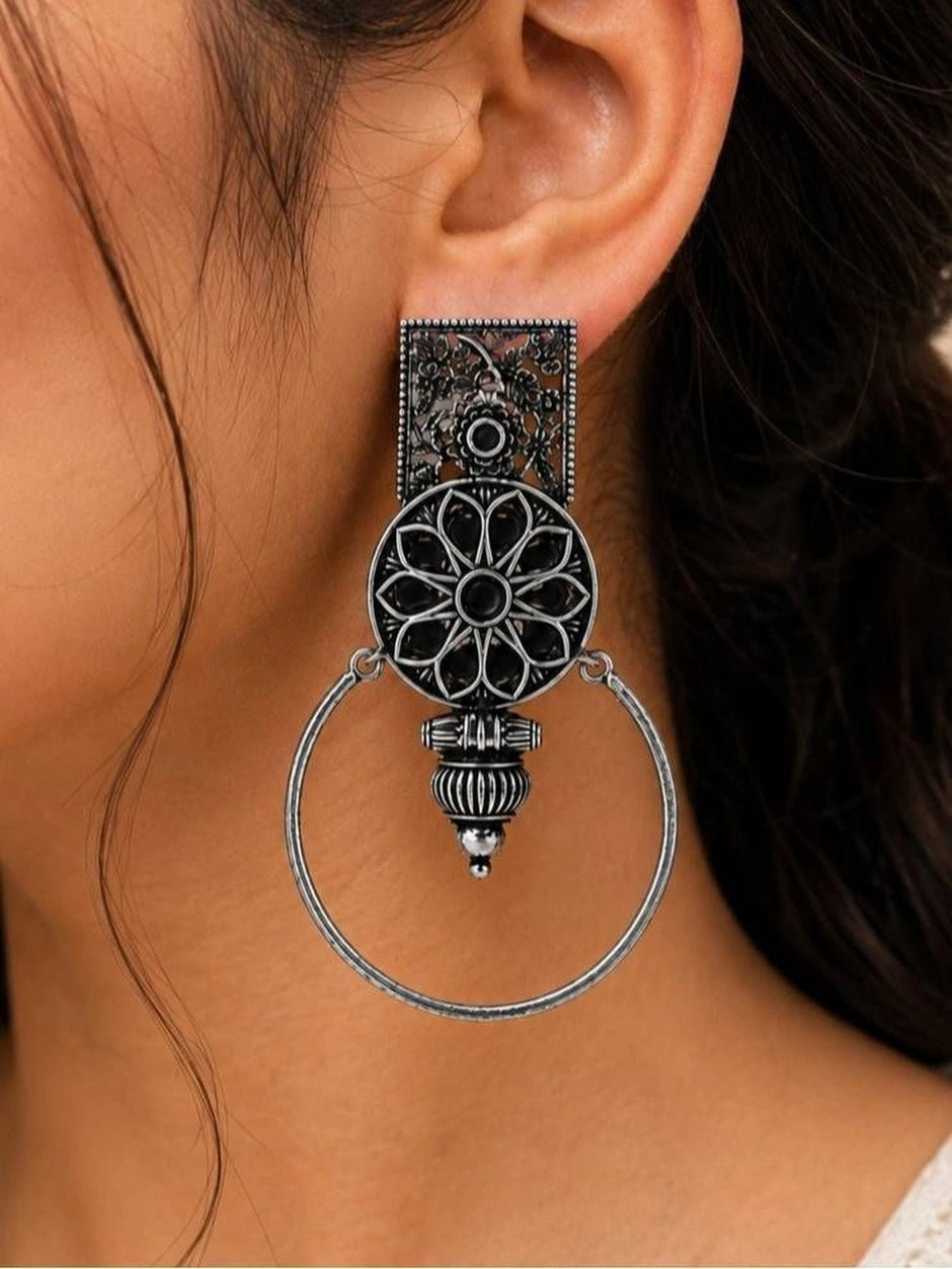 Close-up side view of one oxidised silver floral hoop earring worn on a woman's ear showing full drop length