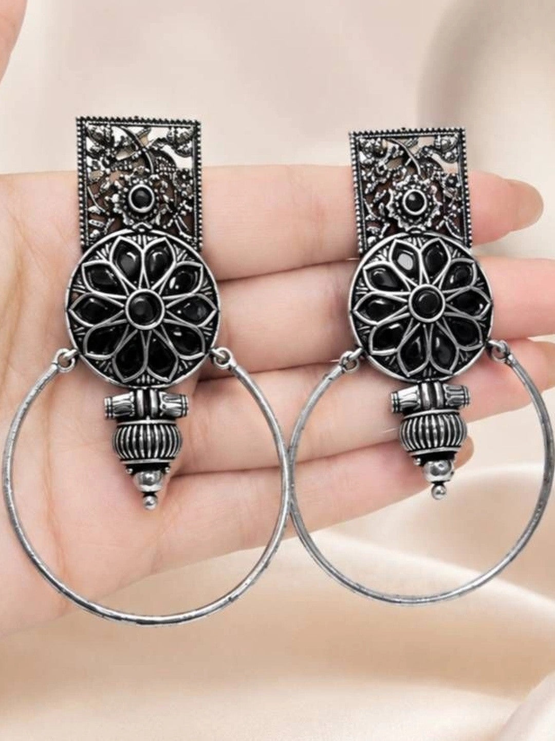 Pair of oxidised silver floral hoop earrings held in an open palm showing black resin stone inlay and ridged bead drop