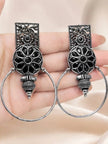 Pair of oxidised silver floral hoop earrings held in an open palm showing black resin stone inlay and ridged bead drop