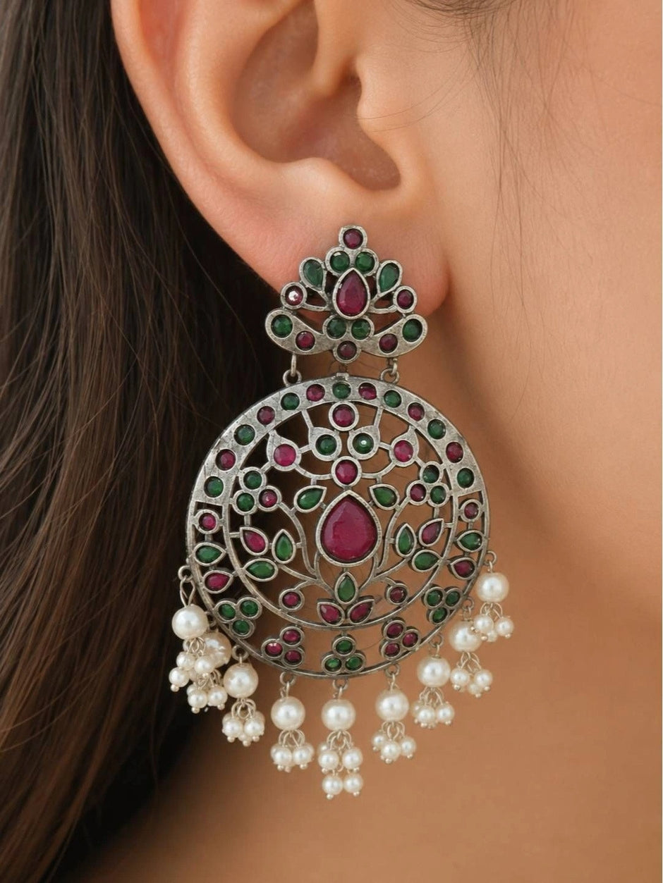 Close-up of a large oxidised chandbali earring worn on a woman's ear, showing floral cutwork disc with pearl drop danglers