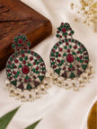 Two oxidised silver chandbali earrings laid flat on white fabric beside a wooden block and small white flowers