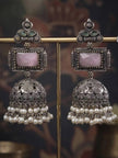 Pair of oxidised silver jhumka earrings with pink stone and pearl drops displayed on a brass bar