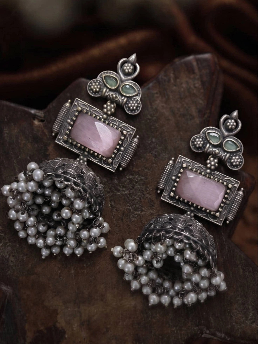 Two oxidised silver jhumka earrings lying on a dark wooden surface showing pearl drop detail