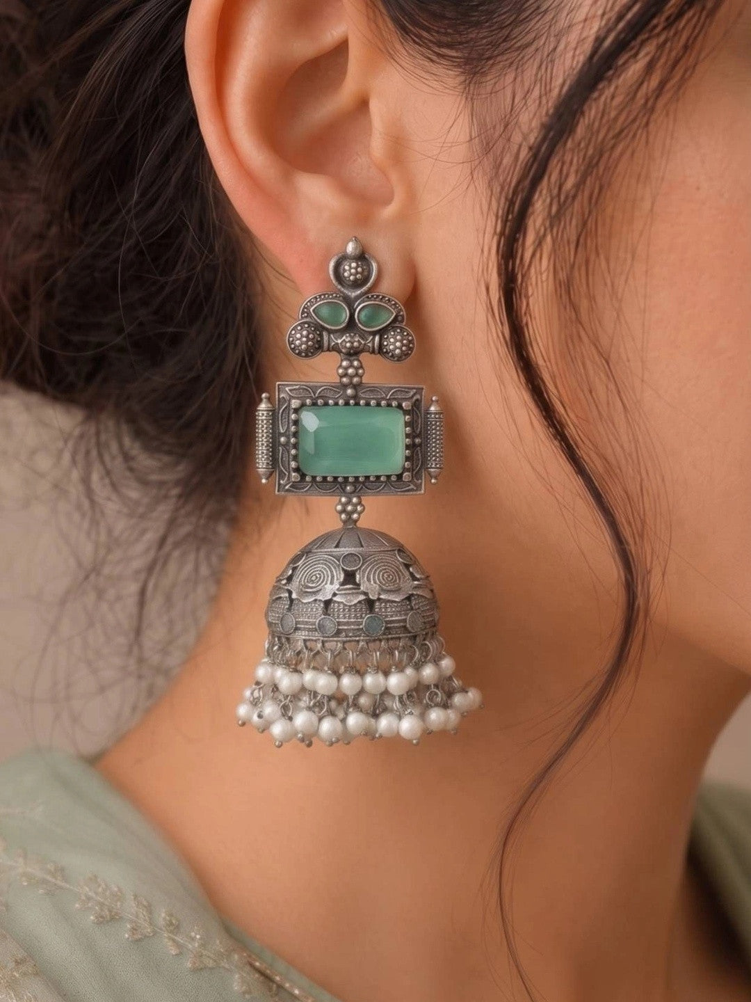 Single oxidised silver green stone jhumka earring worn on a woman's ear with sage green embroidered outfit