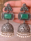 Close-up of oxidised silver jhumka earrings with green stone held in hand showing detailed temple engravings and pearl fringe