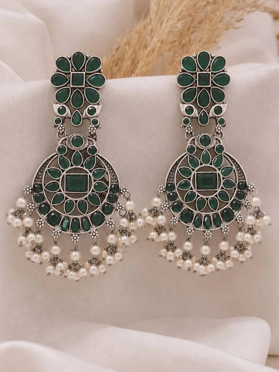 Pair of oxidised silver chandbali earrings with green stones and pearl drops on white fabric