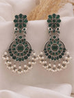 Pair of oxidised silver chandbali earrings with green stones and pearl drops on white fabric