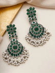 Two oxidised silver chandbali earrings with emerald green stones displayed on cream surface