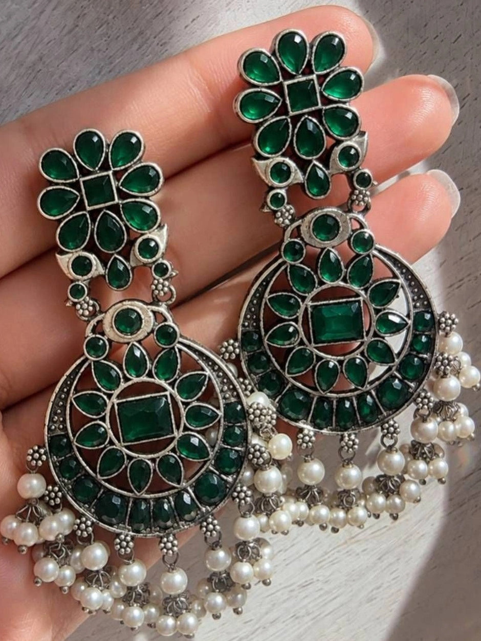 Close-up of oxidised silver chandbali earrings with green glass stones held in palm
